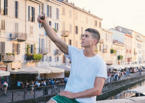 Handsome young man outdoors taking photo or "selfie" with cell phone's camera, in bohemian Navigli area of Milan, Italy