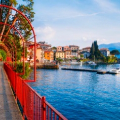 Red garden arch on coastline leading towards the beautiful and historic city of Varenna on the edge of Lake Como in the northern Italian region of Lombardy.